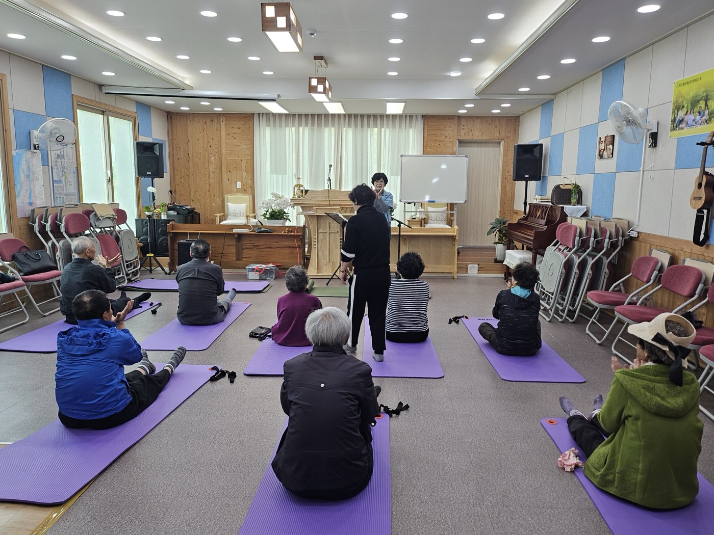 마을 경로당에서 강사와 함께 매트에 앉아 체조하는 어르신들